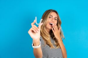 young woman against a blue background holding up her clear aligners